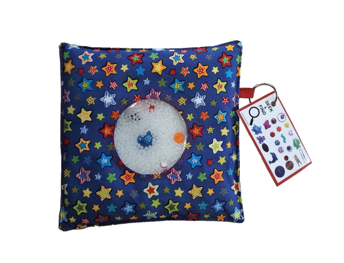 Close-up of a Seek & Find game filled with colorful trinkets and Victory Pellets, showing smooth plastic beads surrounding tiny treasures in a clear sensory pouch.