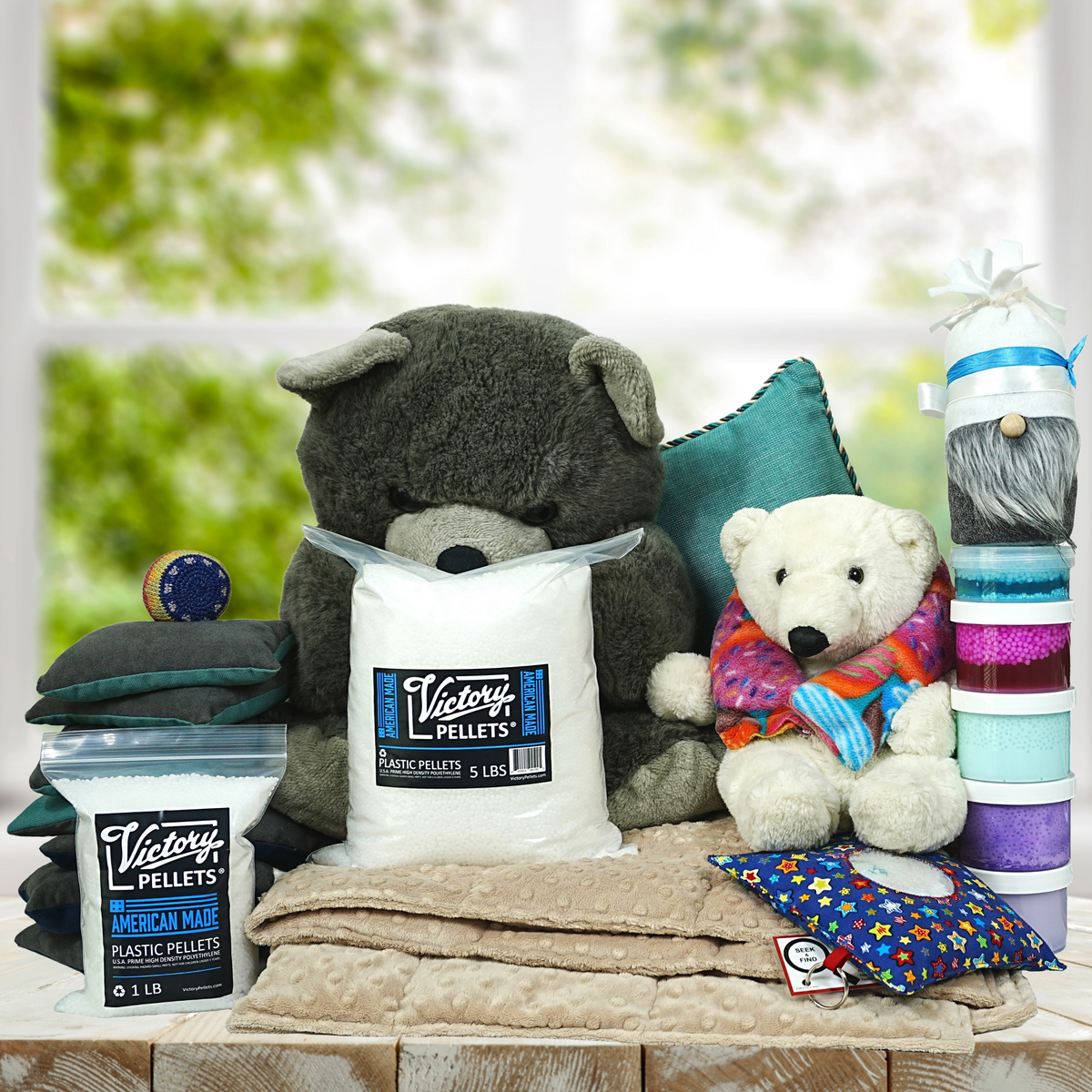 Assorted sensory and comfort items including stuffed bears, weighted blanket, plush pillows, gnome toy, colorful slime, bean bag toss bags, hacky sack, seek-and-find activity, weighted neck wrap, and a 5-pound bag of Victory Pellets–ideal for DIY crafts, stress relief, and cozy play.