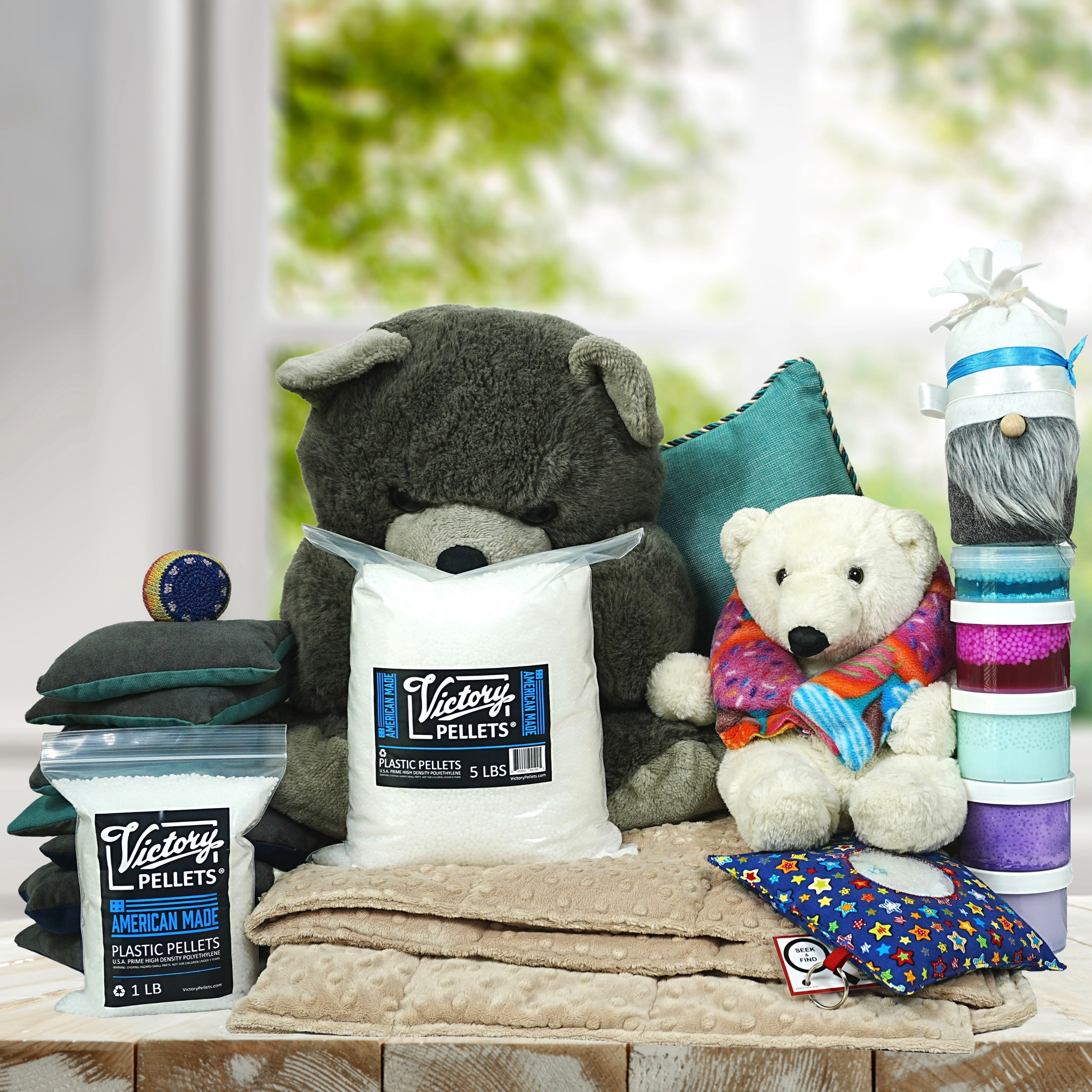 Assorted sensory and comfort items including stuffed bears, weighted blanket, plush pillows, gnome toy, colorful slime, bean bag toss bags, hacky sack, seek-and-find activity, weighted neck wrap, and a 5-pound bag of Victory Pellets–ideal for DIY crafts, stress relief, and cozy play.